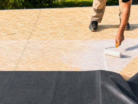 Zur Verklebung der EPDM-Dachfolie auf Holz kommt meist der wasserbasierte Flächenkleber W-1 zum Einsatz. Der Kleber wird gleichmäßig auf den Untergrund gestrichen und die Folie anschließend in die noch feuchte Klebeschicht eingelegt. Auf dem Bild ist zu sehen, wie ein Mann diesen Kleber verteilt.