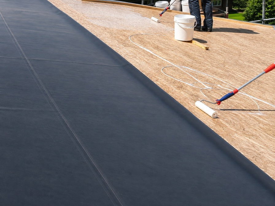 Montage der EPDM Dachfolie auf einer Halle auf OSB-Platten. Der Flüssigkleber wird mit einer Rolle verteilt.